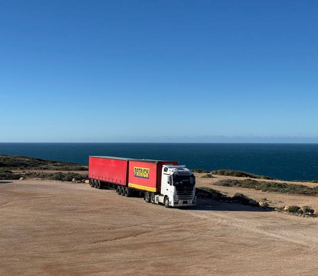 A truck and trailer parked beside the coast road and the ocean